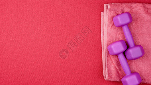 红色新胎垫上的紫色塑料哑铃和粉红色毛巾图片