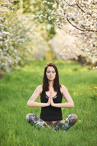 Yogi女孩闭着眼睛坐在春花园的绿草坪上图片