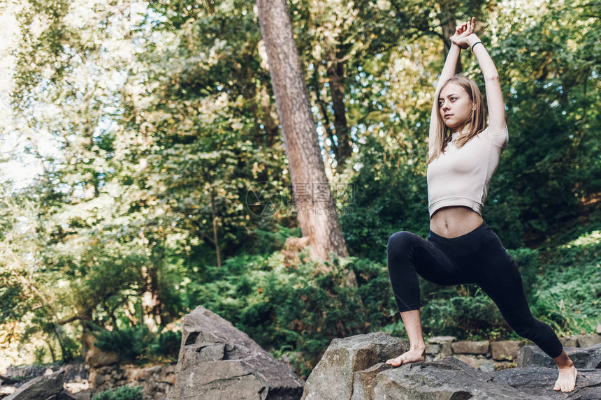 年轻女孩在公园的岩石上做运动时深化瑜伽图片