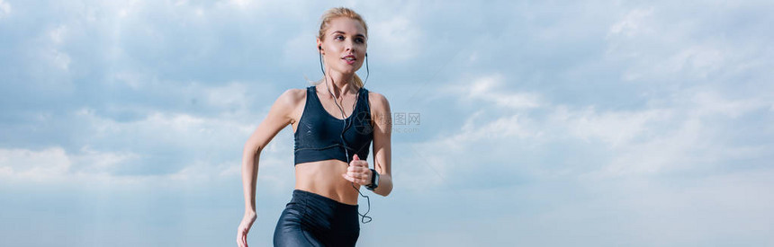 运动型金发女郎在耳机中跑步和听音乐的全景照片图片