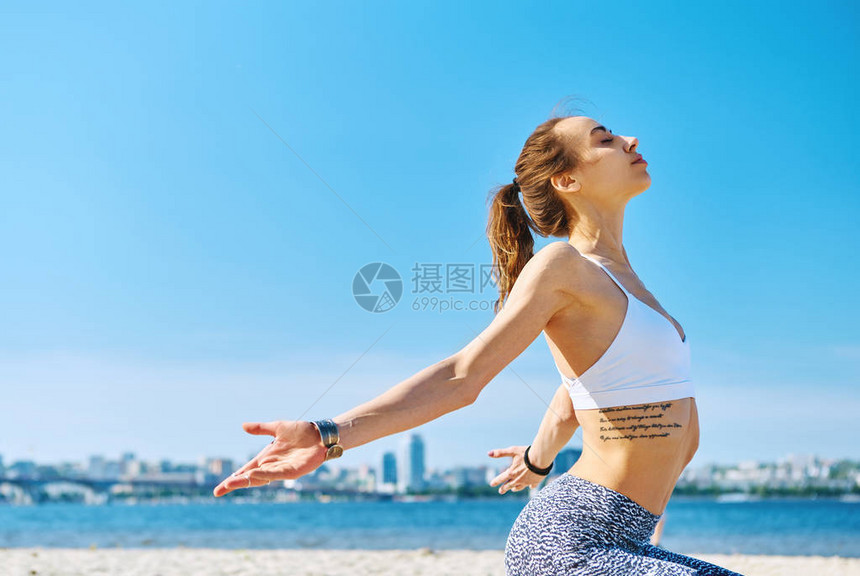 在城市和蓝天背景上举手站在瑜伽体式中的年轻苗条运动女子的户外肖像年轻漂亮的健身女士户外亚洲高加图片
