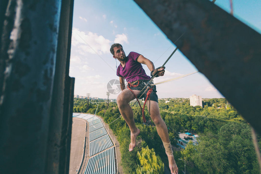 Highliner坐在体育场上方的一条线上一名男子沿着拉长的吊索行走Ropewalker抓住了平衡发展平衡感图片