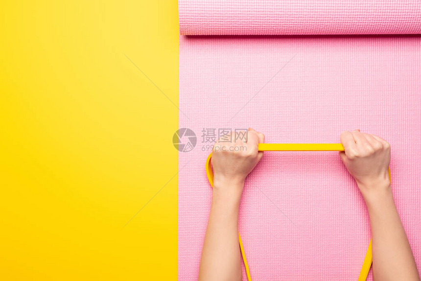 在黄色背景的粉红色健身垫上绑有弹带的妇图片