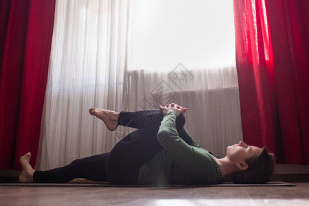 运动妇女在家里客厅休息室躺着并做伸展瑜伽练习图片