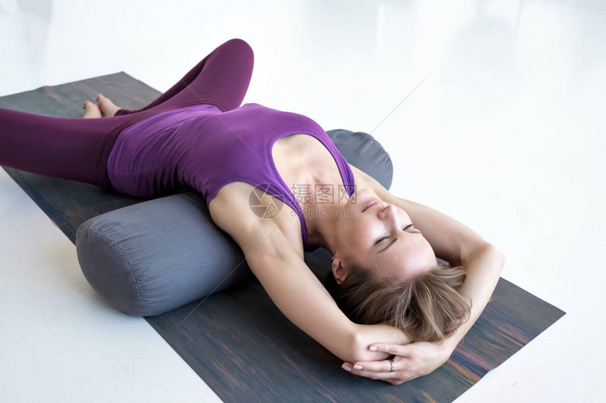 欧洲瘦妇女做瑜伽躺在伸缩蝴蝶锻炼中图片