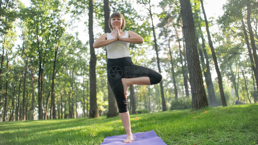 穿着健身服的微笑中年妇女做伸展运动和瑜伽练习的照片在公园草地上的健身垫上冥想和图片