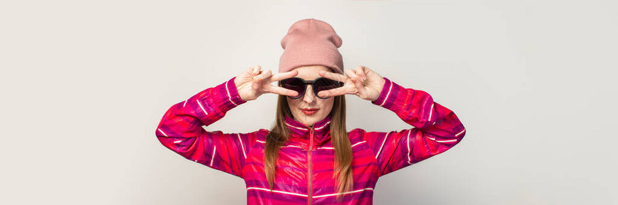 戴眼镜戴帽子和粉色运动夹克的年轻女子做出很酷的手势图片