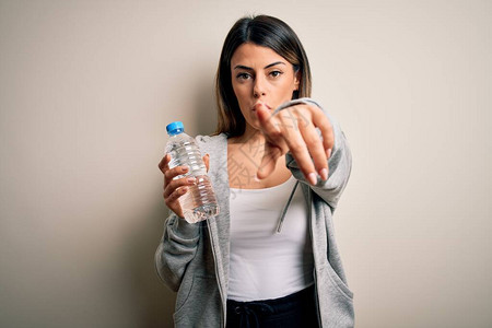 年轻漂亮的黑发运动型女人在孤立的白色背景上喝瓶水图片