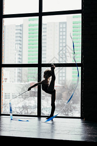 Gymnast使用丝带进行锻炼一个女孩在明亮的窗口背图片