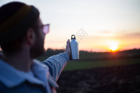 拿着铝瓶装水的人手在日落的背景下图片