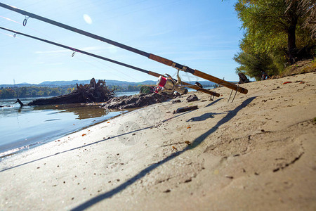 两根钓鱼竿安装在位于河流沙滩上的架子上图片