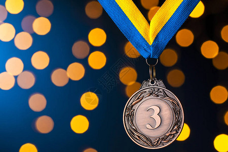 第三名赛跑者铜奖章挂在一条带子上在蓝色背景和金色布基的图片