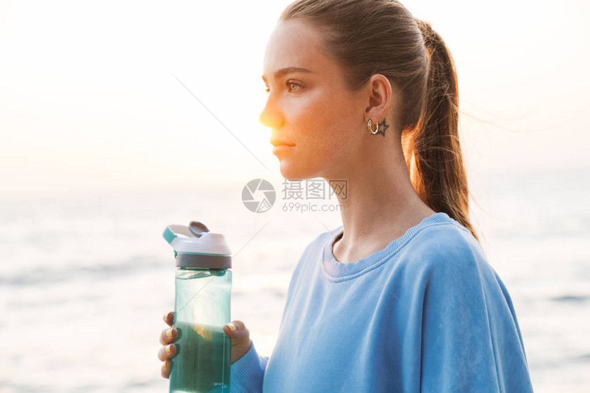 一位美丽的年轻红发美女健身女在海滩饮水上露天面的画面图片