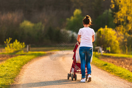 红婴儿车中的年轻母亲和儿童在日落前在农村地区户外行走图片