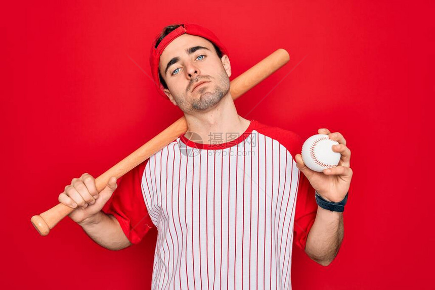 蓝眼睛打棒球的年轻英俊运动员戴着帽子拿着球和蝙蝠自信地表现在聪明的面孔上图片