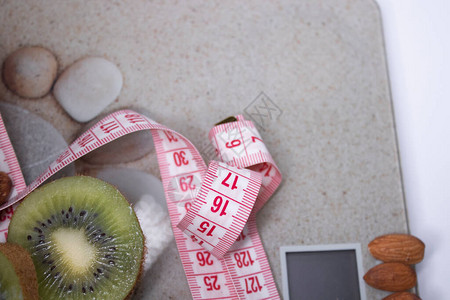 暴瘦符米色浴室秤上的红色卷尺苹果猕猴桃和杏仁饮食与健康生活减肥运动理念顶视图复制空间孤背景