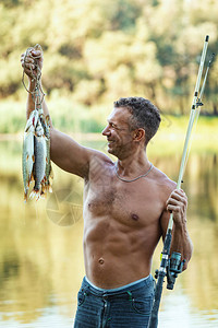 一个年轻英俊的满意渔夫将捕获的鱼抓在钩子图片