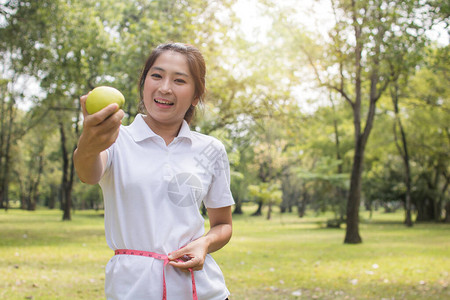 亚洲妇女在公园锻炼和运动持有绿苹果以换图片