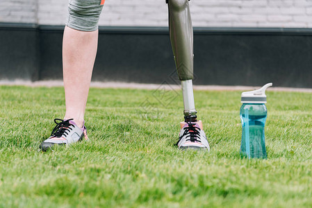 残疾人运动女运动员在街上草地体育瓶旁站图片