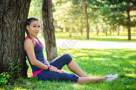 运动妇女坐在草地上靠在树底的公园一棵图片