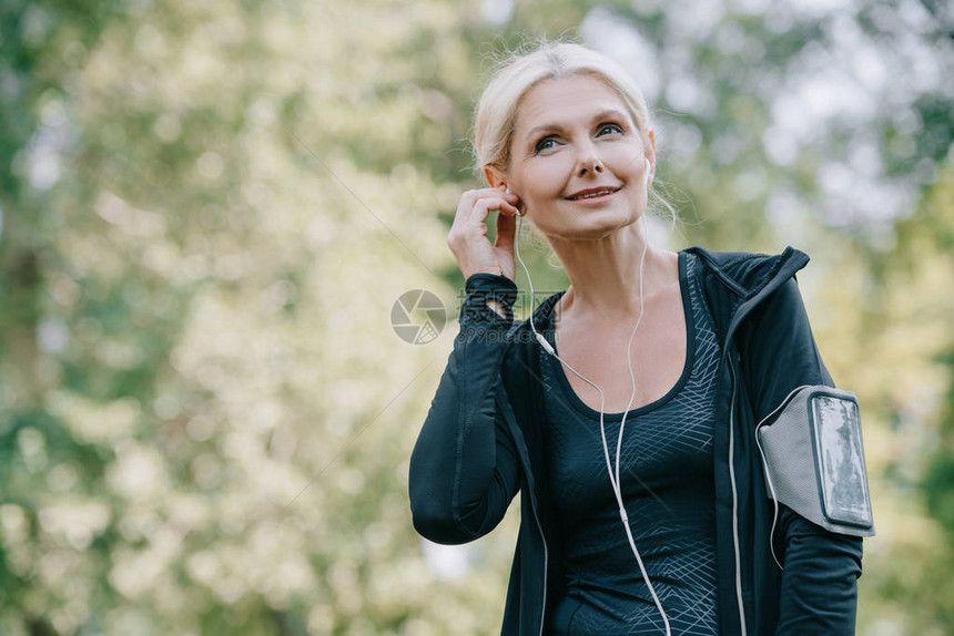 微笑着的成熟运动女运动员在听耳机音图片