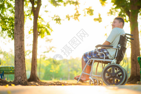 坐在市公园轮椅上的年轻残疾的亚洲男子日落图片