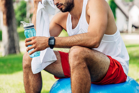 坐在健身球和擦汗时拿着运动瓶子的胡须男图片