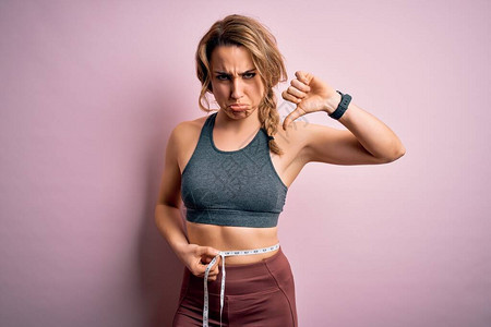 年轻的金发女运动员穿着运动服在腰部用卷尺控制体重图片
