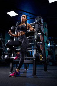 摸着辫子Srtong女人肌肉发达的身体靠在健身房的杠铃上背景图片