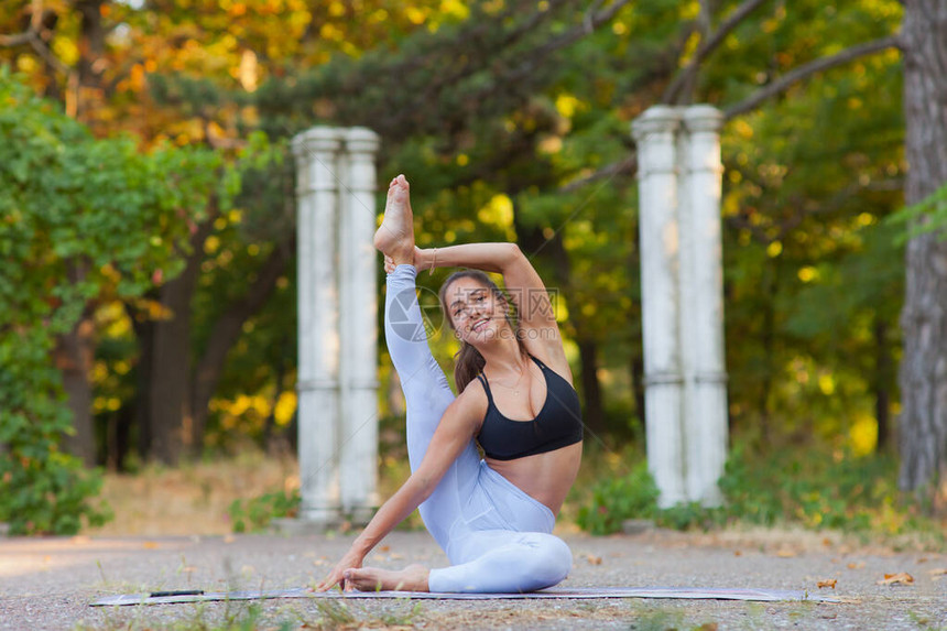 运动女练瑜伽在夏日明亮的绿园上露面图片