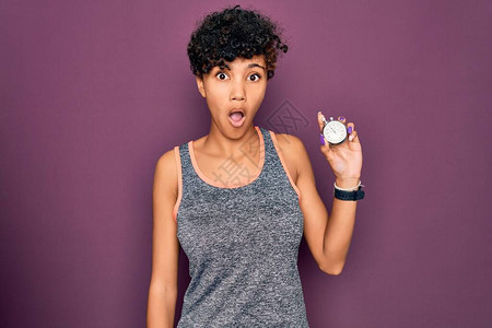 年轻漂亮的非洲裔美国运动型女在紫色背景下拿着秒表图片