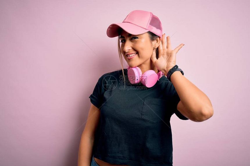 身戴训练帽和穿粉红色背景耳机的年轻健身运动女子图片