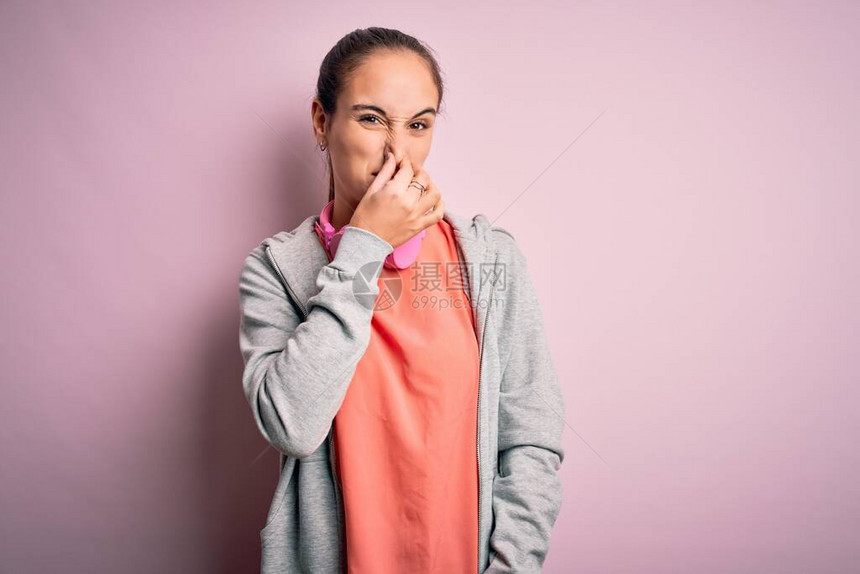 美丽的运动型女人在做运动时用耳机在粉红色的背景上听音乐图片