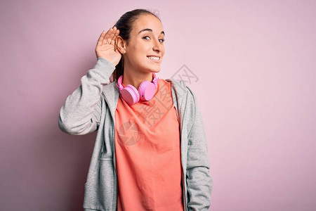 从事运动的美丽体育女郎在粉红背景上用耳机聆听音乐图片