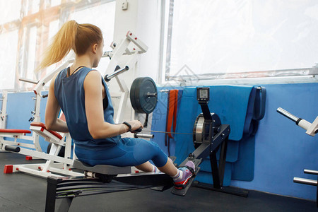 年轻的运动女在健身房的划船机上进行体育锻炼后视图健美健康的生活方式体图片