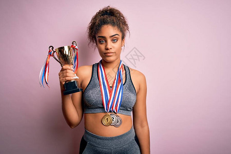 年轻美国体育女青年在粉红背景上打运动奖章和奖杯图片