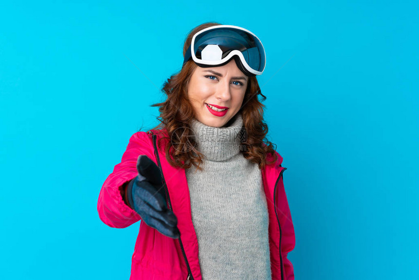 有滑雪眼镜的滑雪女人在隔绝的蓝墙上握手图片