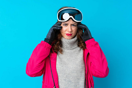 在孤立的蓝墙上戴滑雪眼镜的滑雪妇女对某事感到不愉快和沮丧图片