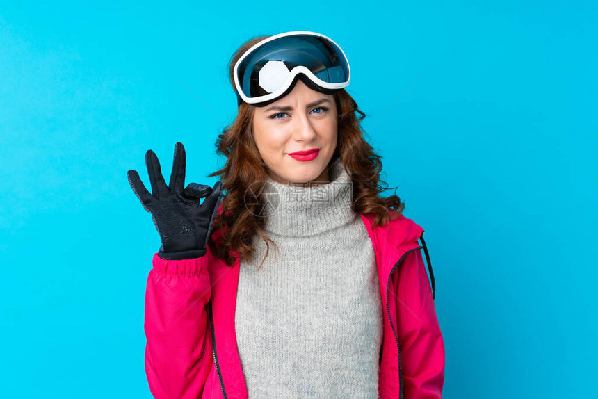穿着滑雪眼镜的滑雪女人在隔绝的蓝色墙壁上举起手来表图片
