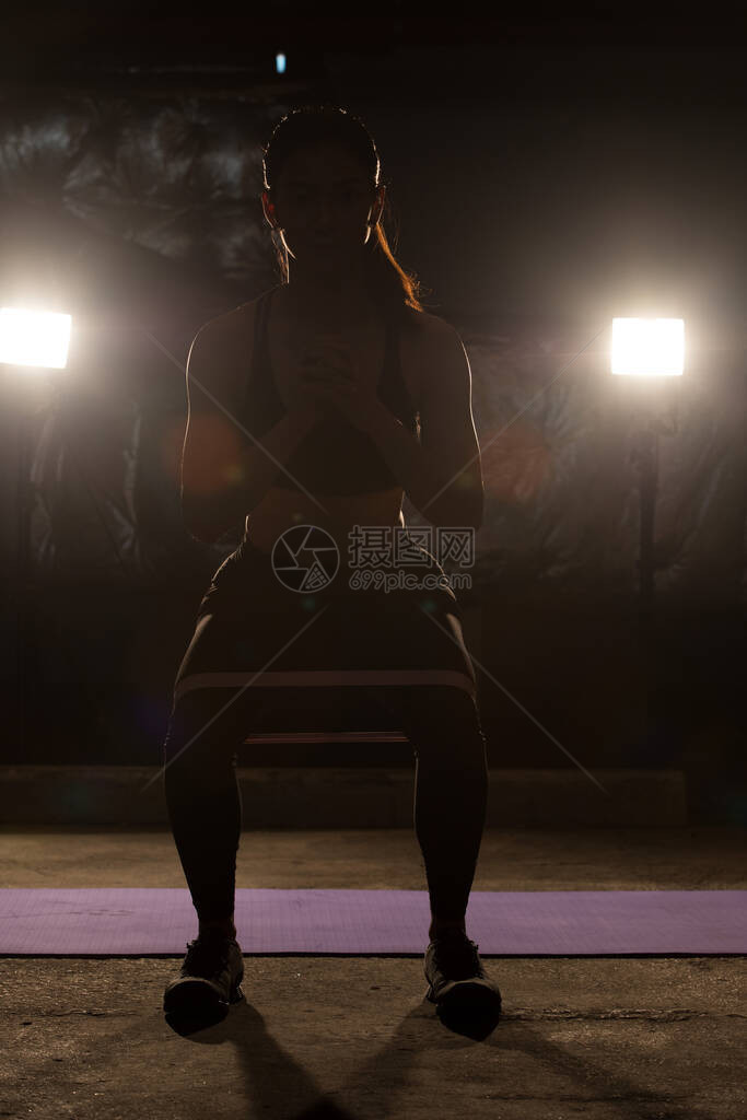 亚洲苗条健身女锻炼伸展腿手臂阻力带在雾烟黑暗背景低曝光环境图片
