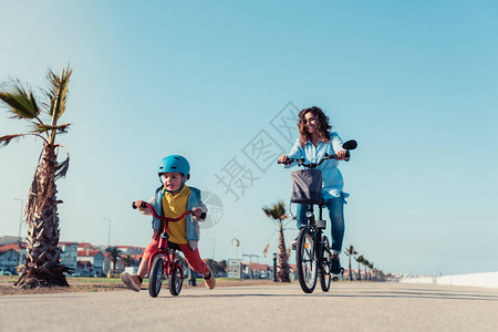 小孩在城市公园骑着平衡车和妈一起骑自行车图片