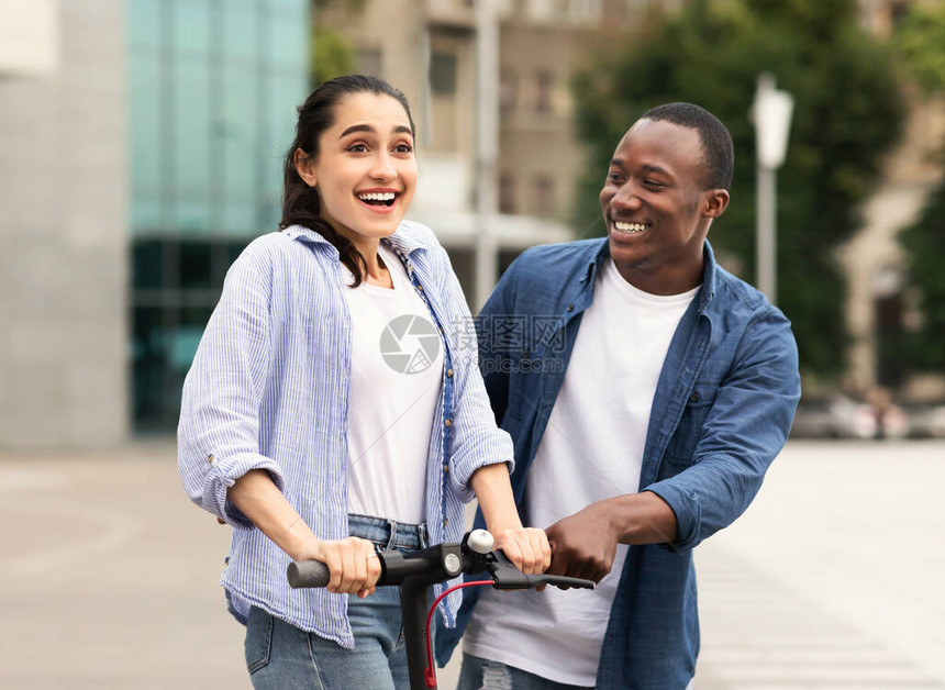 黑人男子的肖像教他兴奋的女朋友如何在城里骑电动脚踏图片