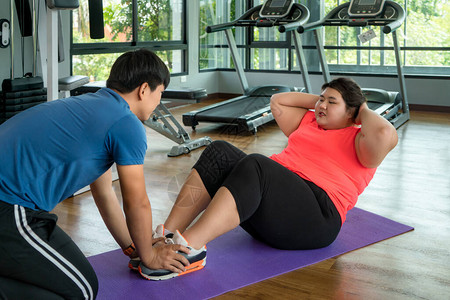 两名亚洲教练男子和超重女子在现代健身房一起锻炼图片
