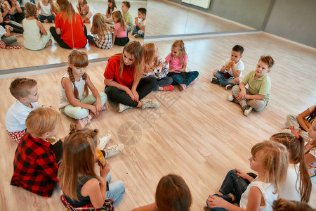 一群坐在地板上的小舞者围在她们的女舞蹈老师身边图片