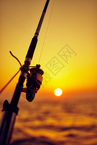 在日落日出和海洋地平线的船上钓鱼竿图片