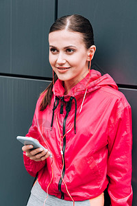 微笑的女运动员在街上用耳听器和智能图片