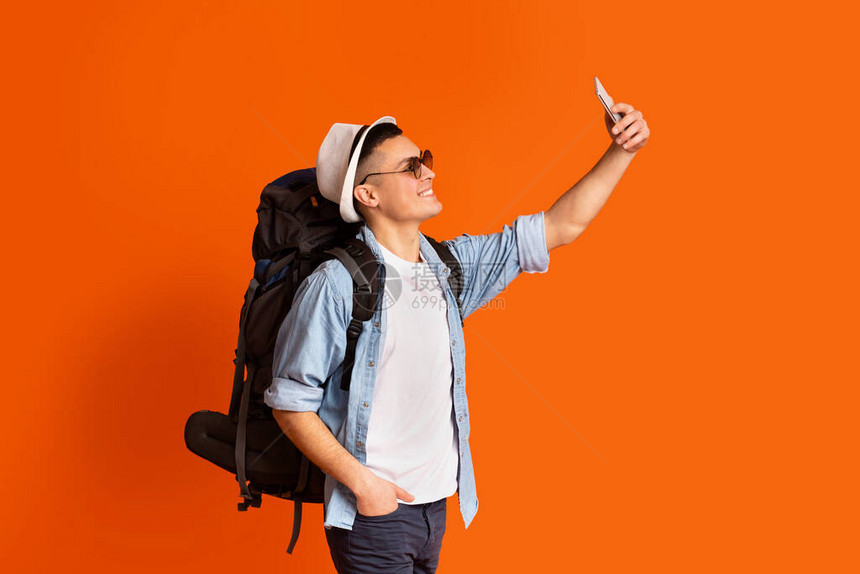 用智能手机在橙色背景上行走时背带自拍的图片