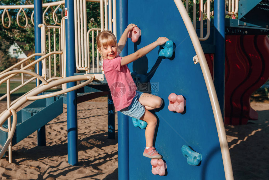快乐微笑的学龄前小女孩在夏日户外操场上攀岩快乐的童年生活方式概念孩子们的季图片