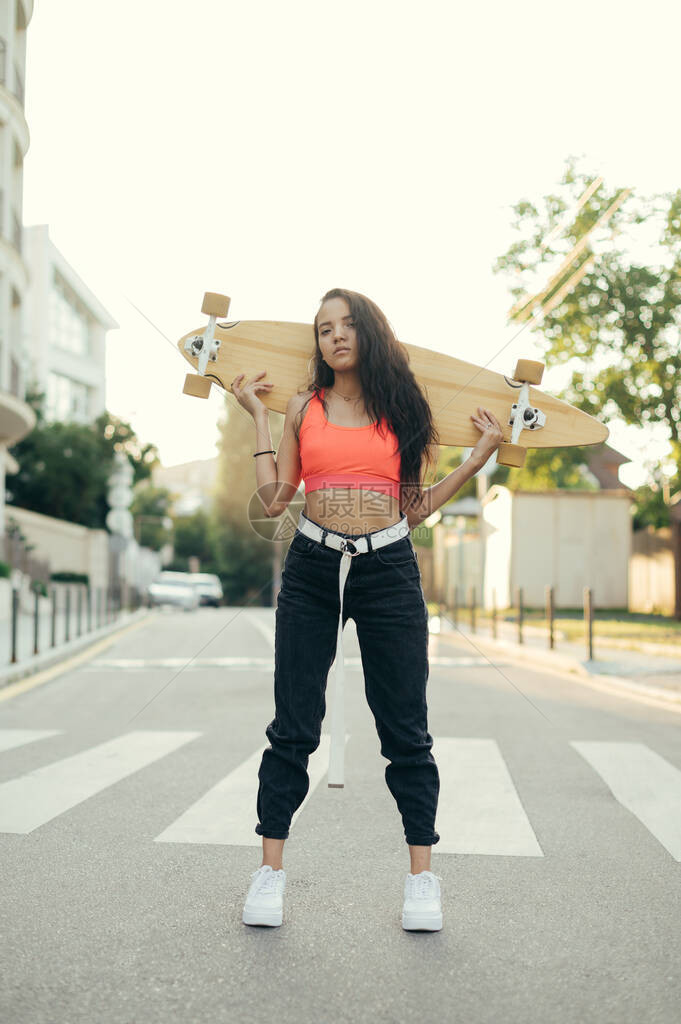 有吸引力的西班牙裔女人的肖像在时髦的街头服饰摆在相机与滑板在手中肩后背着长板的漂亮街头女图片