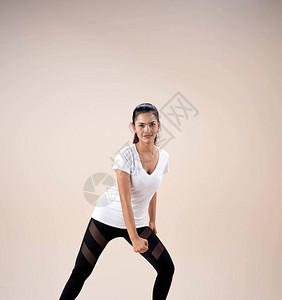 身穿运动服站立双脚的年轻美女跪在腿边拳头跳舞锻炼充图片